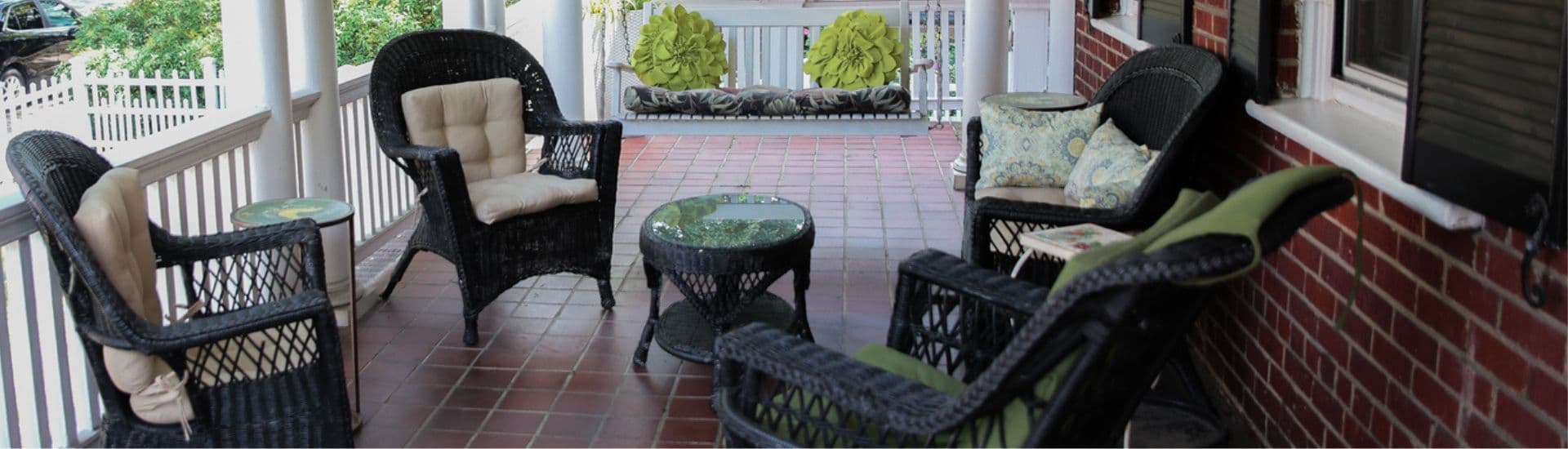A cozy porch featuring wicker chairs, a glass-top table, and decorative cushions.